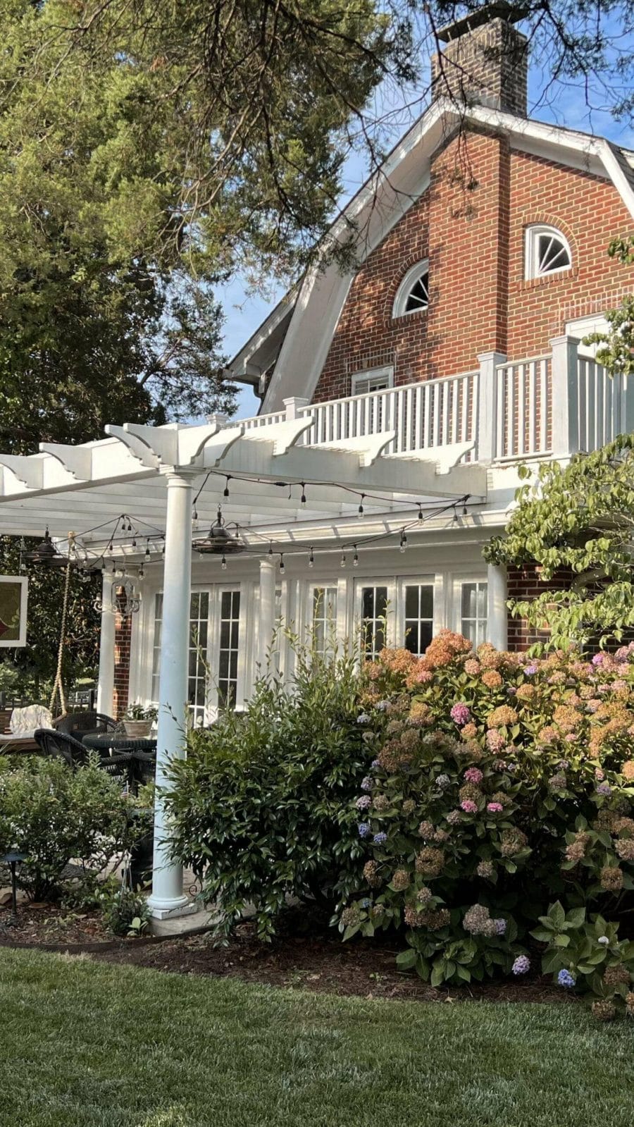 Contemporary garden design featuring a white wood pergola with dark wicker furniture, surrounded by lush hydrangeas in pink and blue.