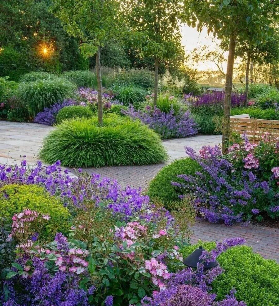 Flower bed design showcasing vibrant purple and pink flowers, layered ornamental grasses, and a circular brick pathway for accessibility.