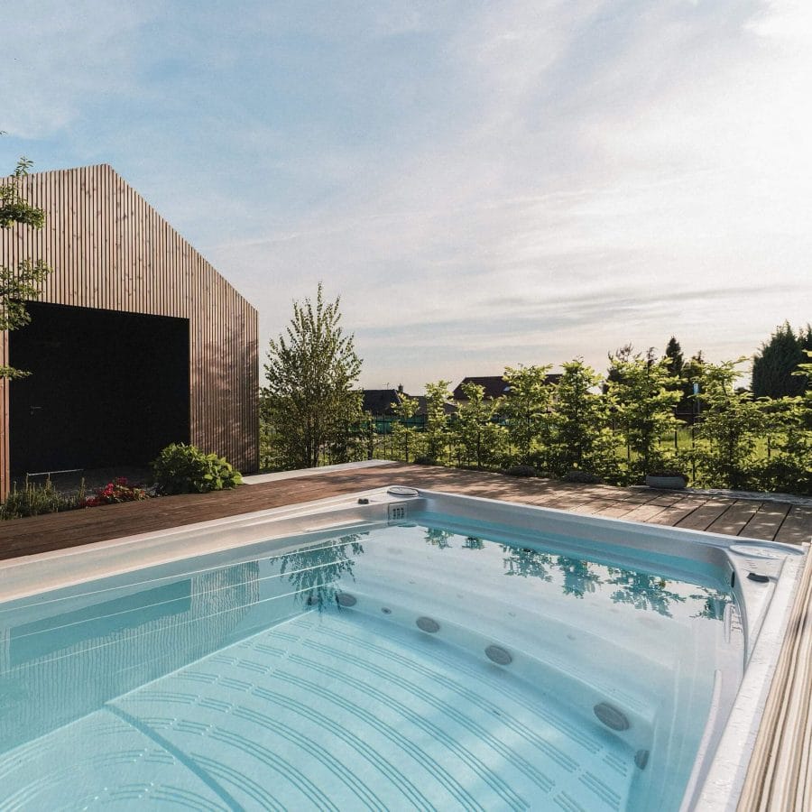 Modern swim spa measuring 3x2 meters, surrounded by hardwood decking and lush greenery, designed for relaxation and exercise.