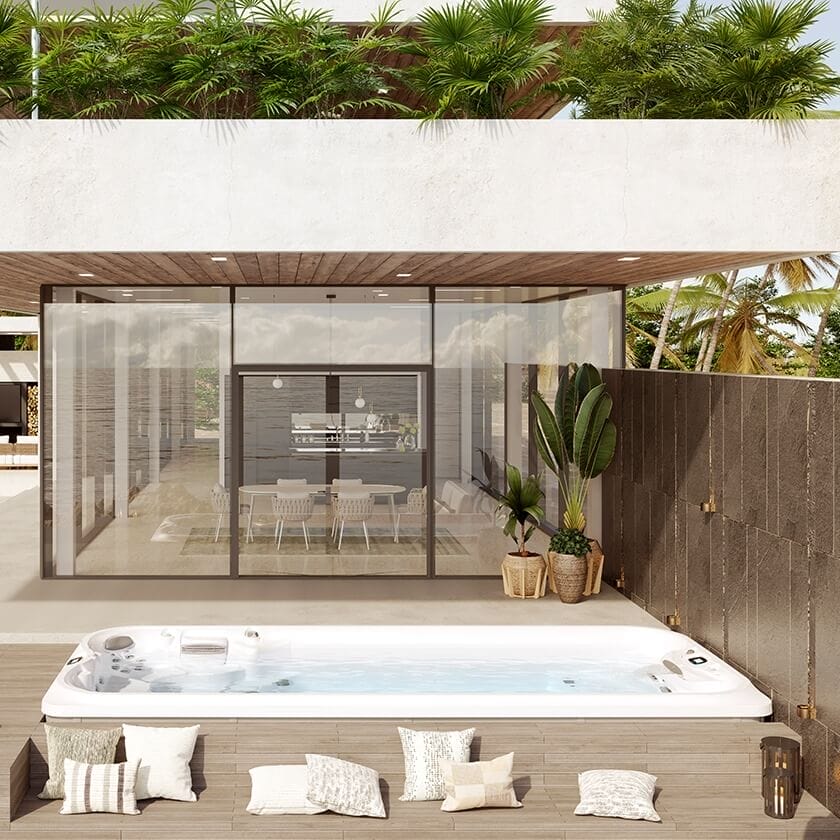 Outdoor swim spa with a rectangular white acrylic shell on a wooden deck, surrounded by patterned pillows and lush tropical landscaping.